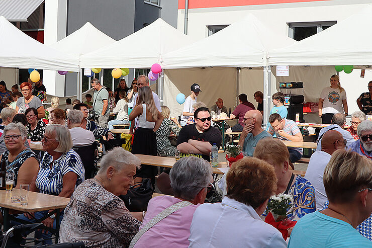 Viele Menschen sitzen an Holztischen zusammen und reden.