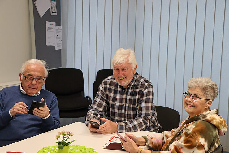 Zwei Männer und eine Frau betrachten ihre Smartphones.