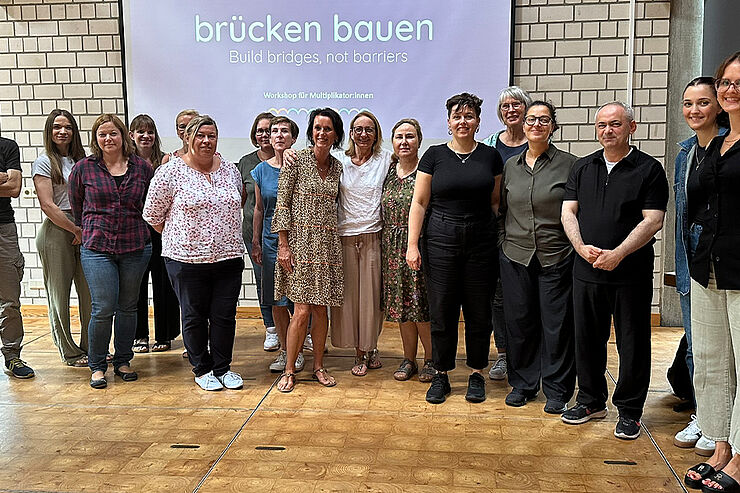 Eine Gruppe Menschen steht nebeneinander vor einer Leinwand mit der Aufschrift "brücken bauen".