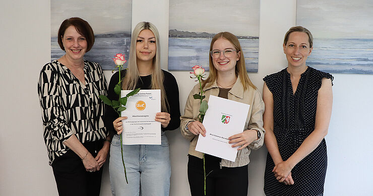 Vier Frauen stehen nebeneinander und halten Dokumente in der Hand.