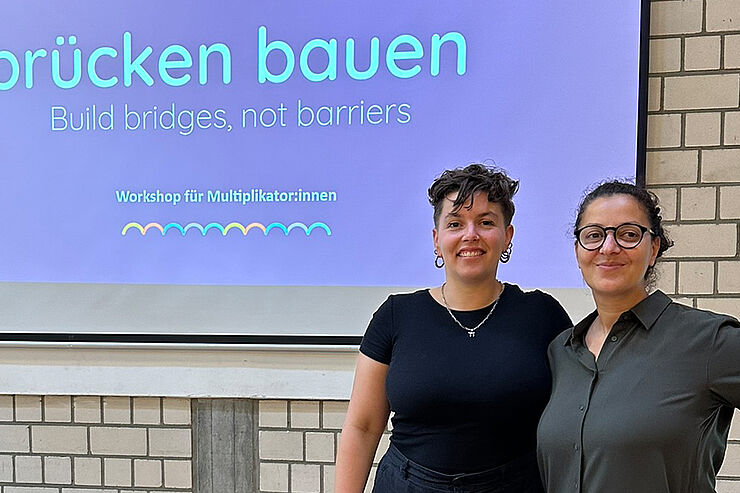 Zwei Frauen stehen vor einer Leinwand mit der Aufschrift "brücken bauen"