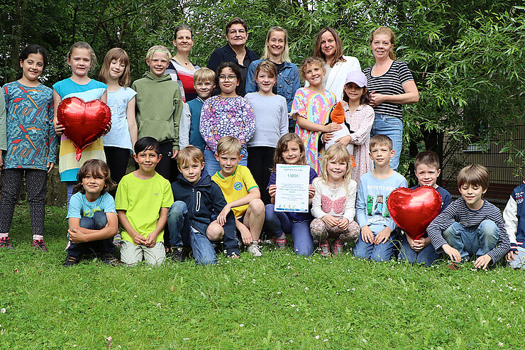 Eine Gruppe von Kindern und Erwachsenen steht und hockt auf einer Wiese.